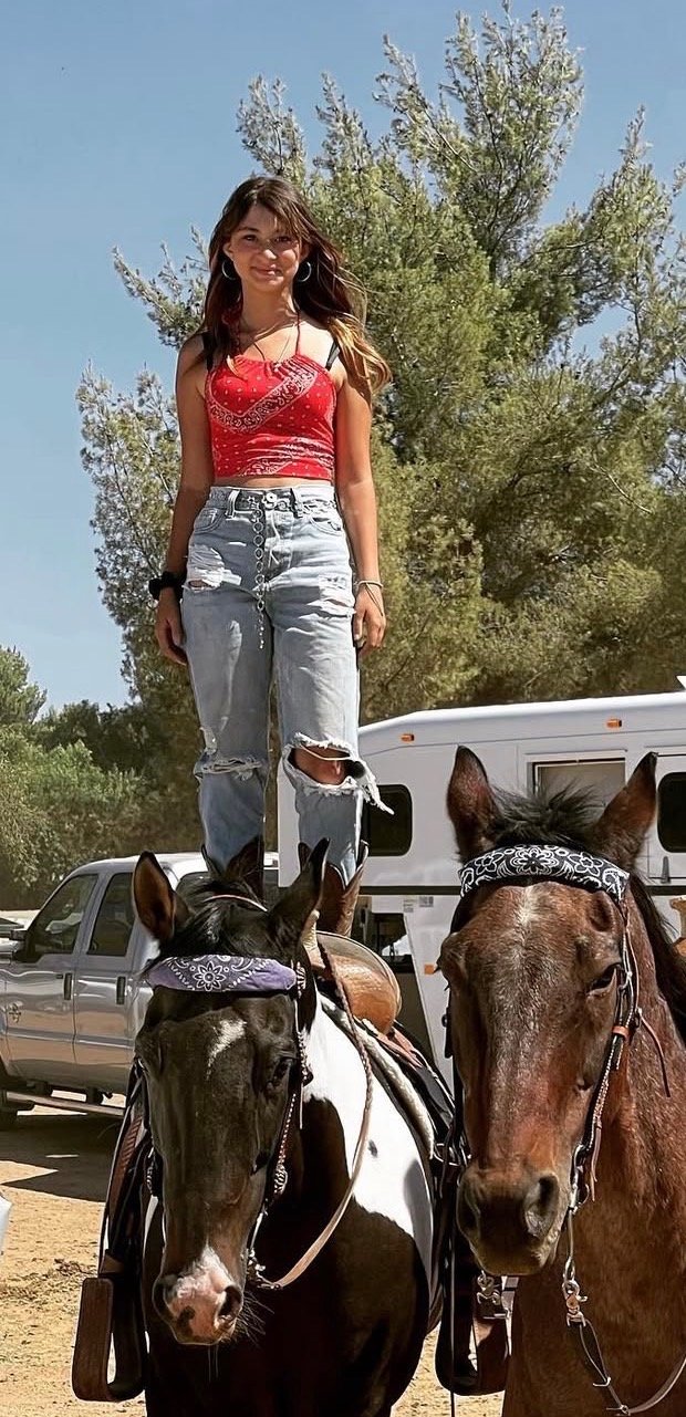 Apani D., Snake School scent detection dog trainer, standing on two horses at a ranch